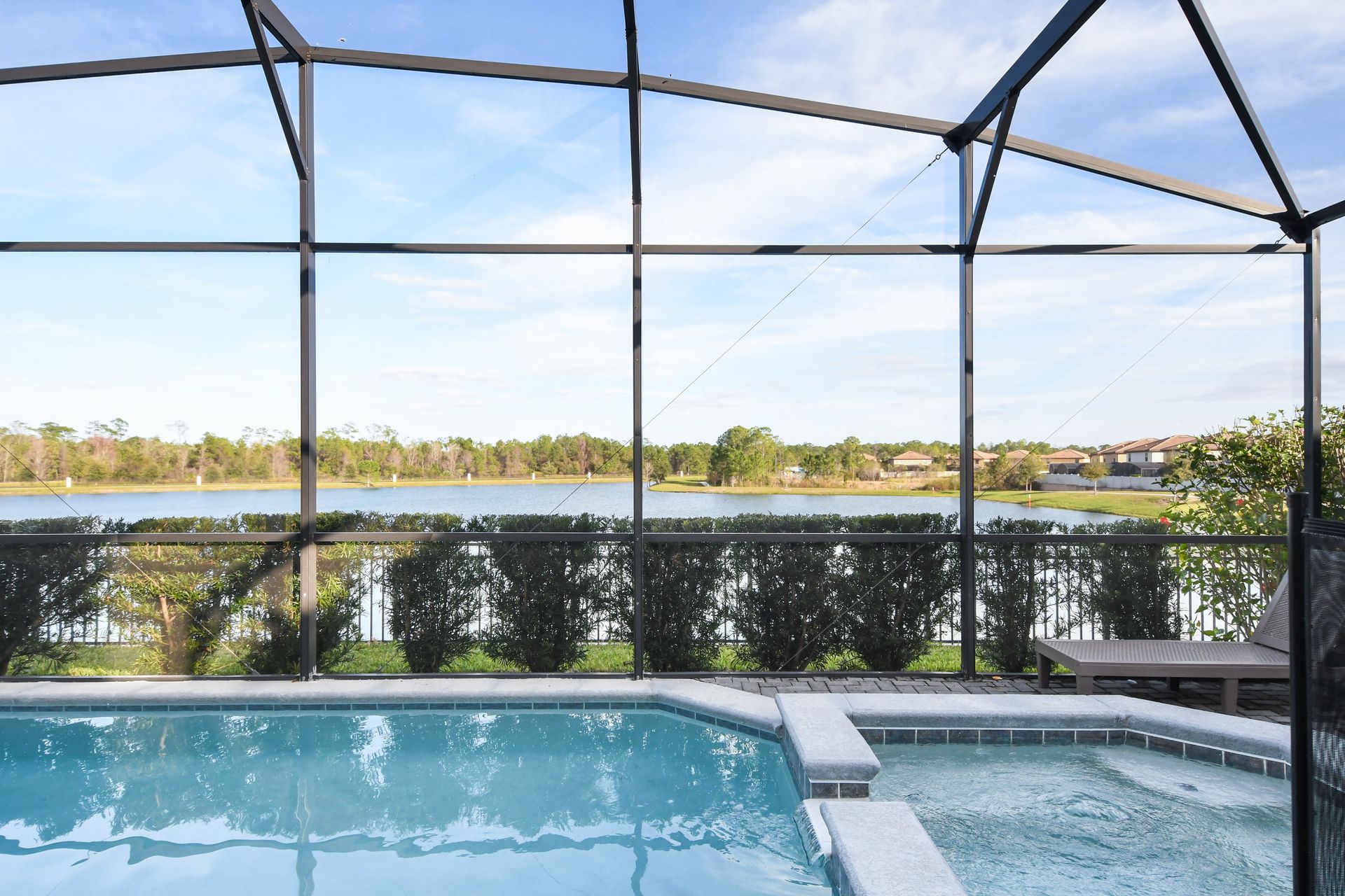 Screened-in pool and spa overlooking a serene lake with lush greenery views.