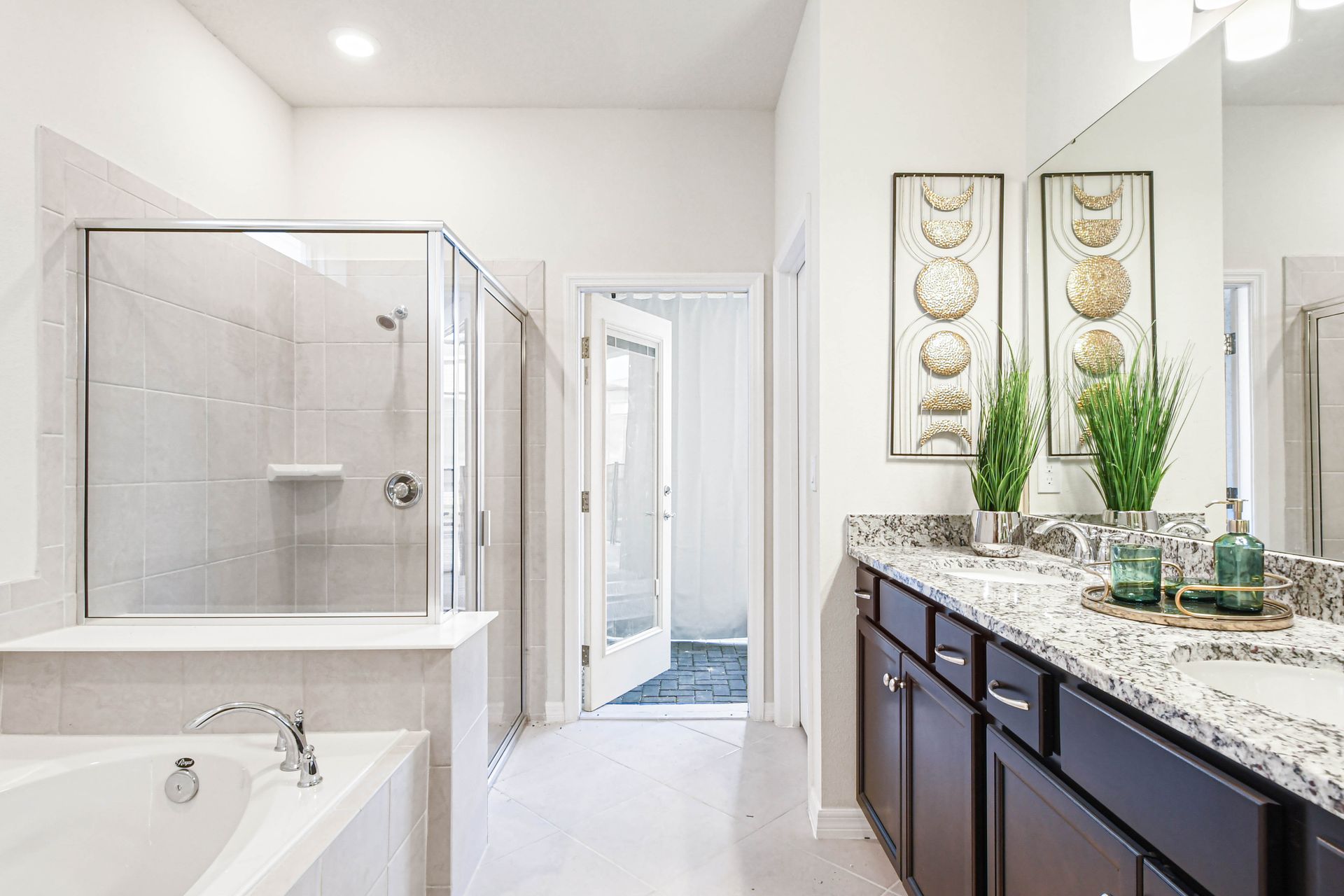 Elegant primary bath with double vanity, soaking tub, walk-in shower, and patio access