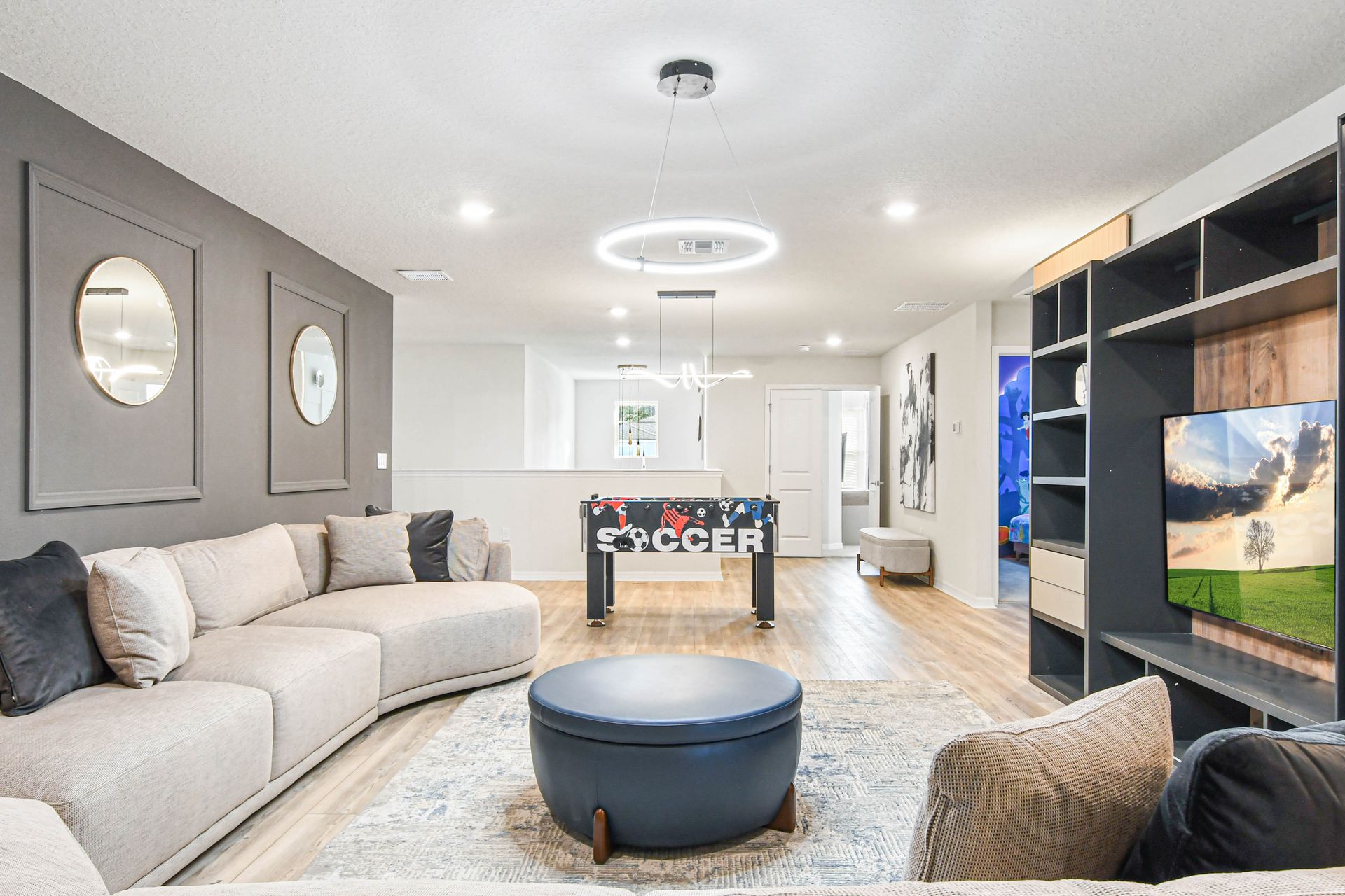 Modern media lounge with large sectional, foosball, sleek lighting, and TV wall unit