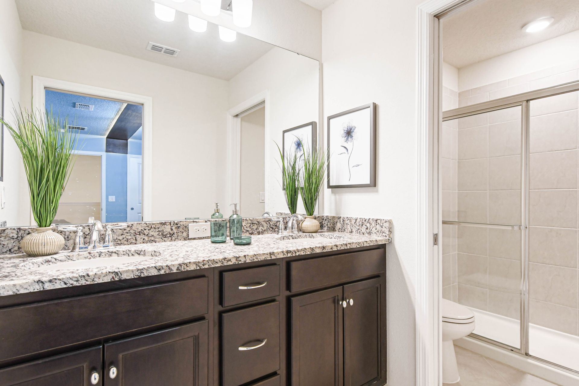 Bright bathroom with double sinks, granite counters, and a spacious glass-enclosed shower