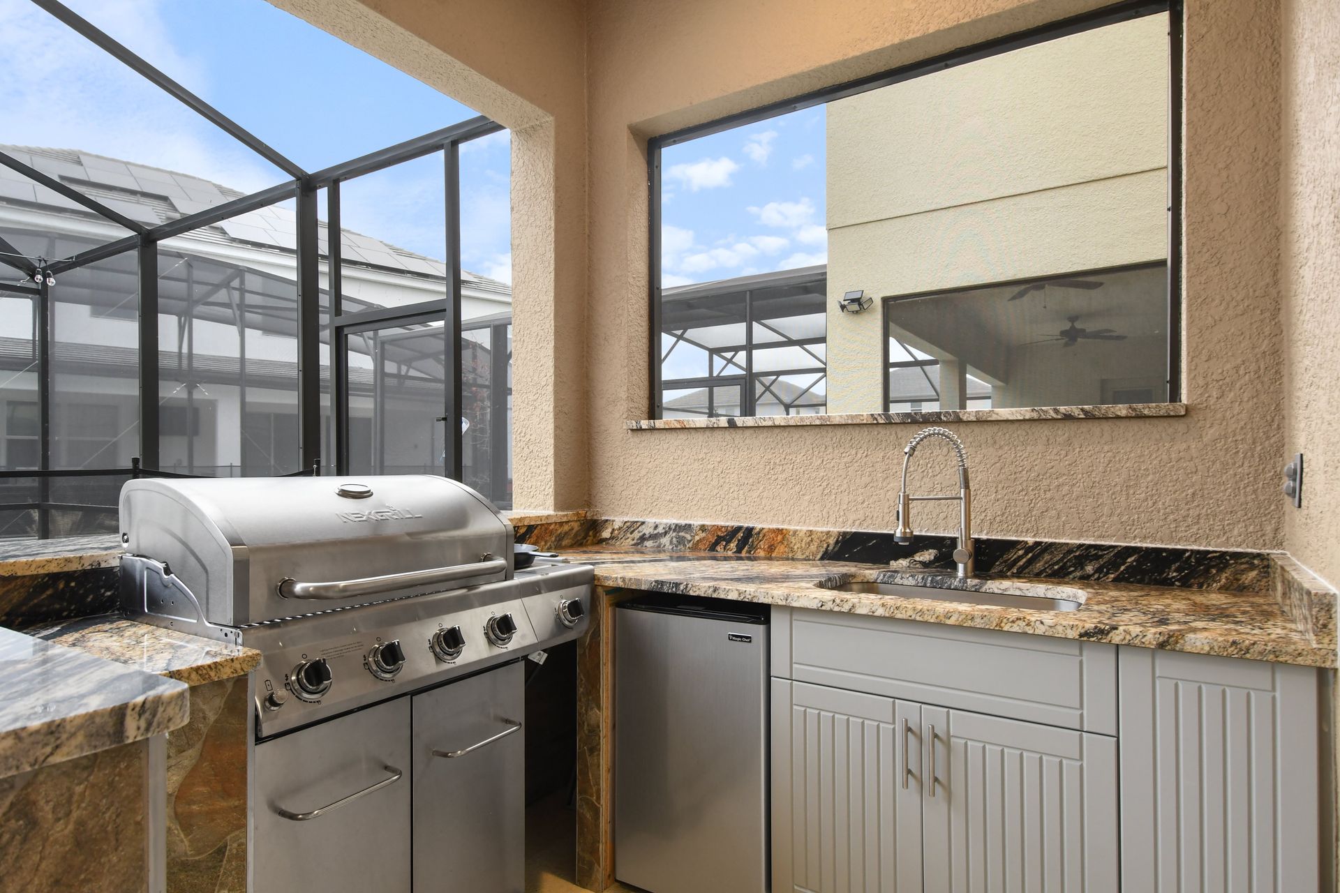 A beautiful outdoor kitchen and grilling area with a view of the screened-in pool and spa. 