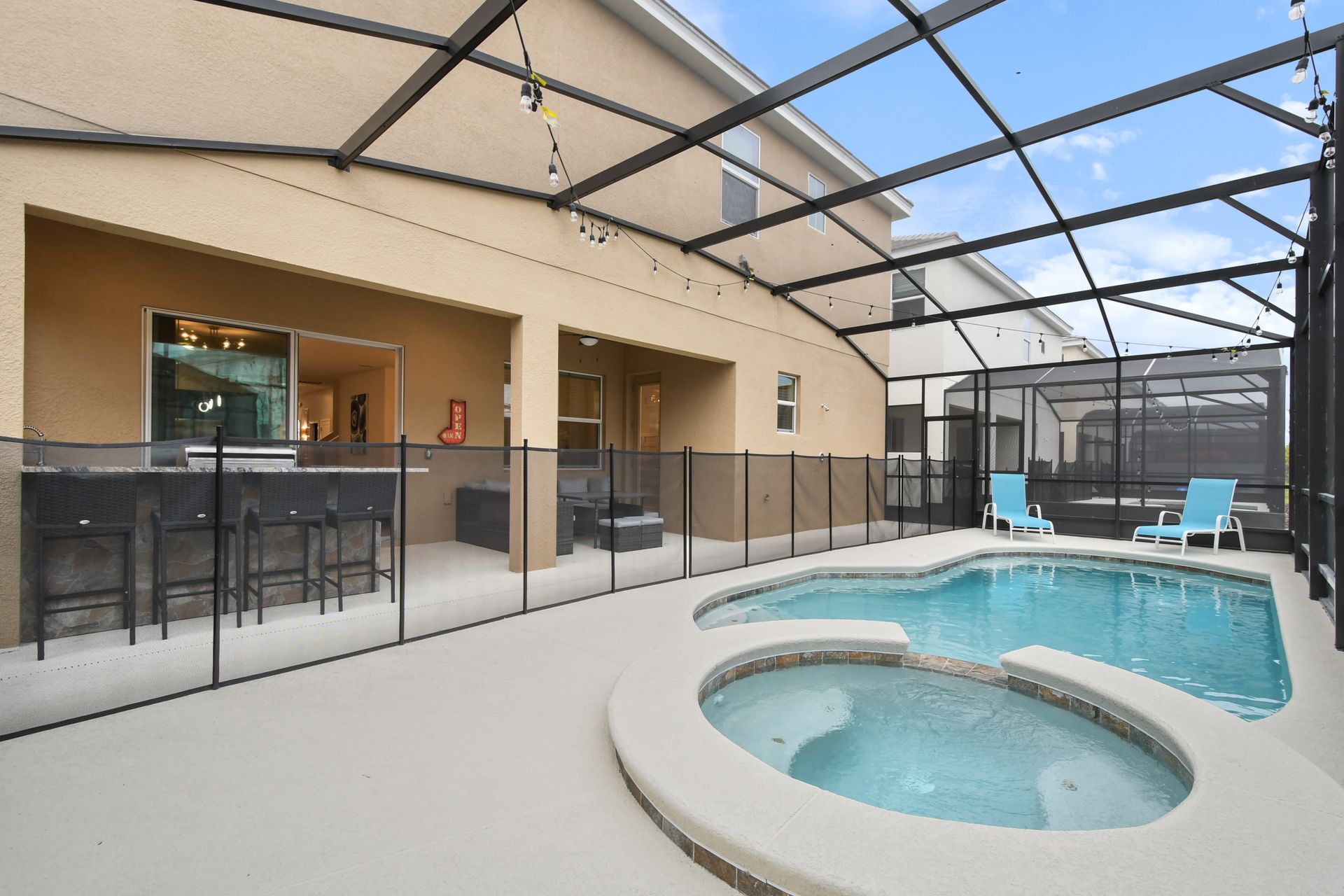 Screened-in private pool and spa with lounge seating and string lights for relaxation.