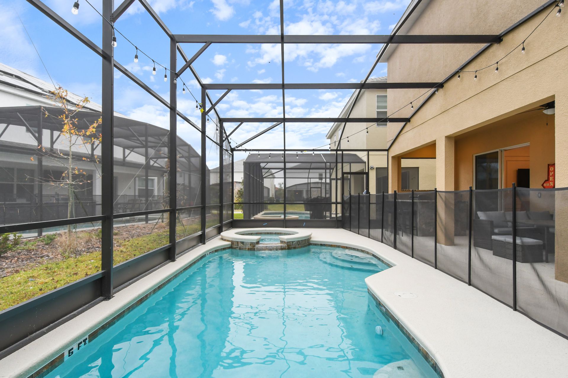 Screened-in private pool and spa with lounge seating and string lights for relaxation.