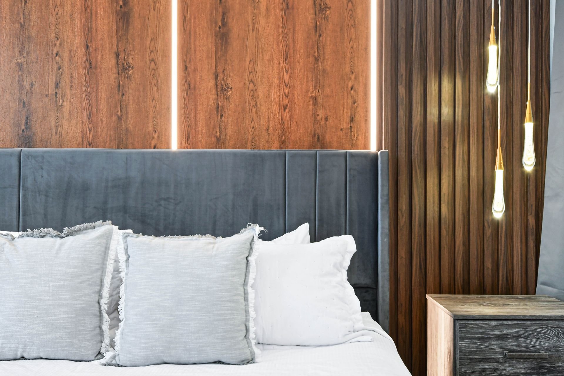 Modern bedroom with cozy bedding, warm wood accents, and elegant pendant lighting.