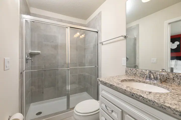 Modern bathroom with granite vanity, glass shower, and sleek tile finishes throughout.