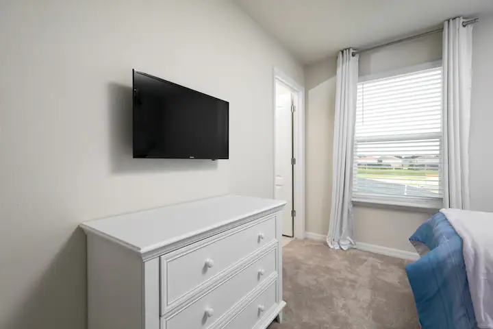Bright bedroom with ensuite bath, flat-screen TV, and charming white accents.