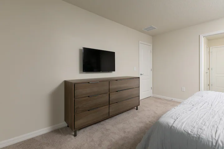 Cozy bedroom with smart TV, modern wood dresser, and soft neutral tones.