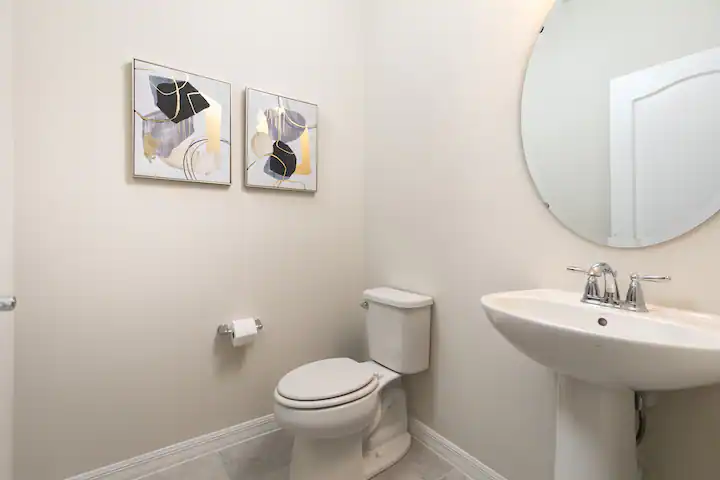 Clean and modern half bath with pedestal sink, abstract art, and soft lighting.