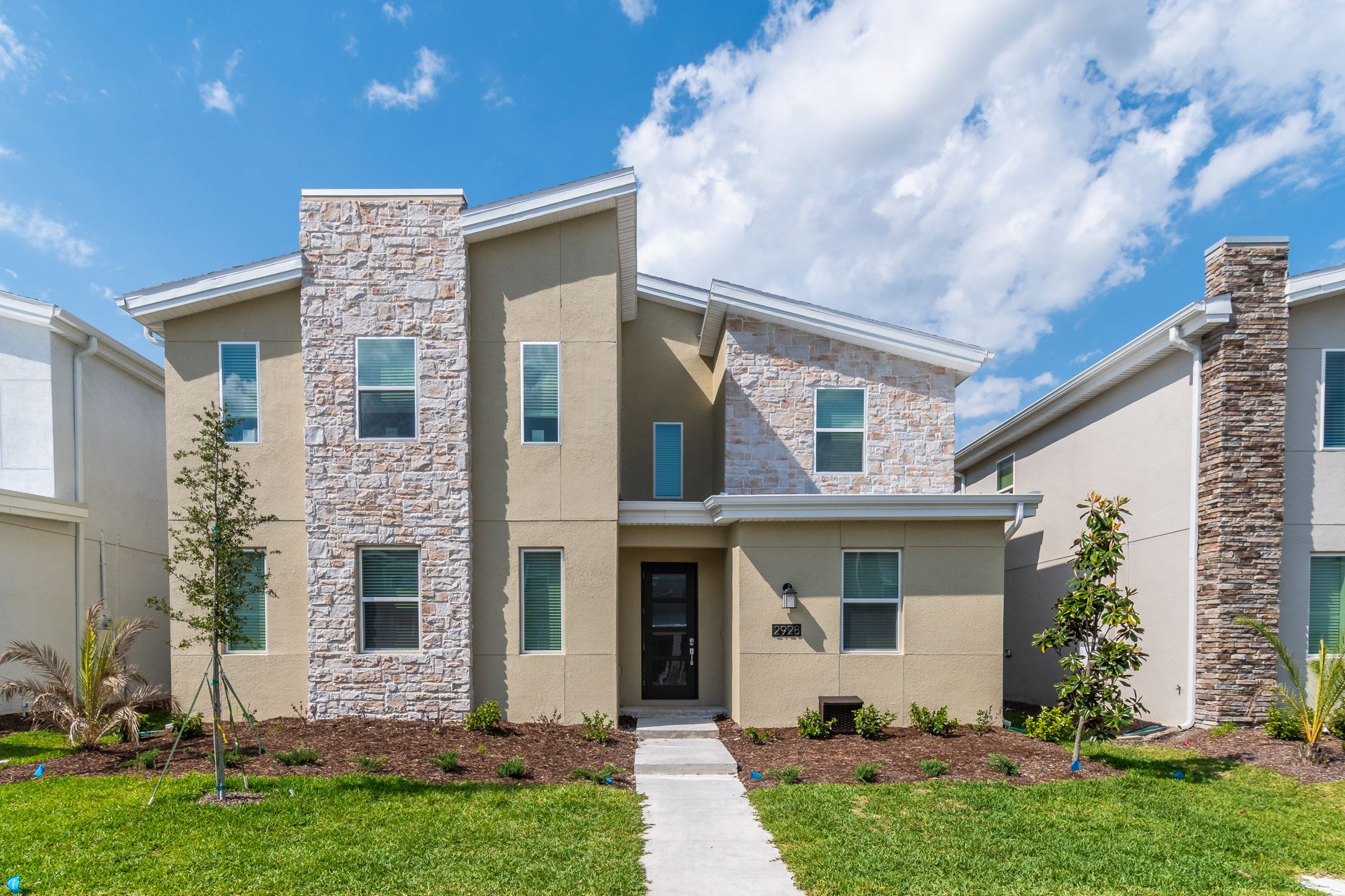 Modern spacious vacation villa with stone accents, fresh landscaping, and sunny charm
