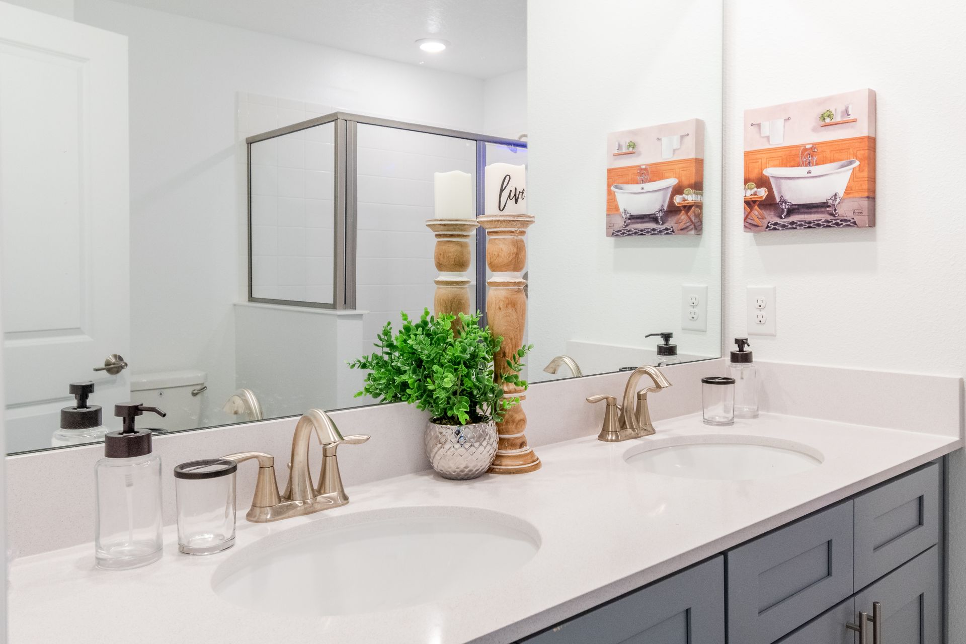 Fresh modern bathroom with double sinks, walk-in shower, greenery, and warm decor
