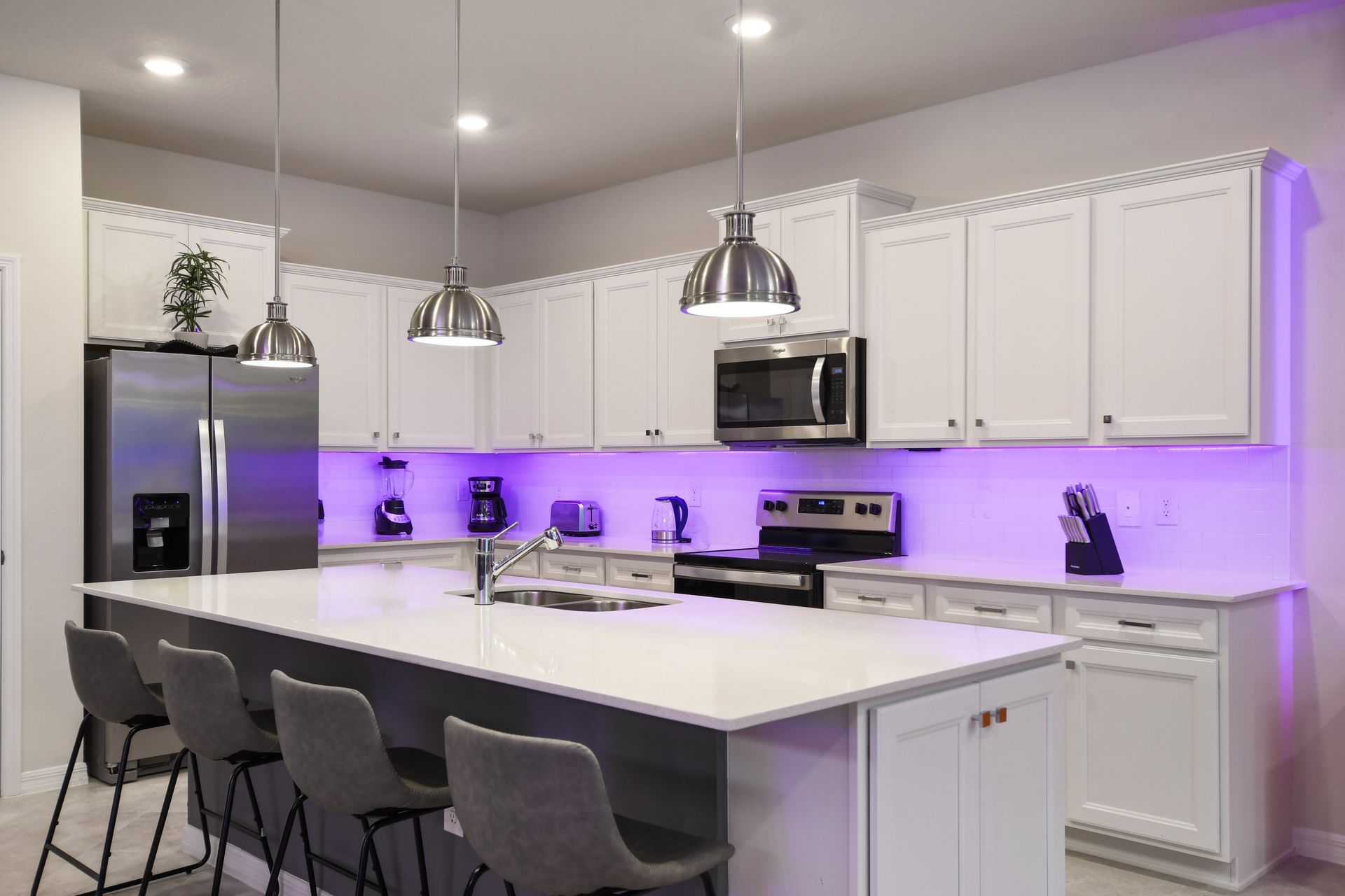 Modern kitchen with stainless steel appliances, island seating, and LED lighting.