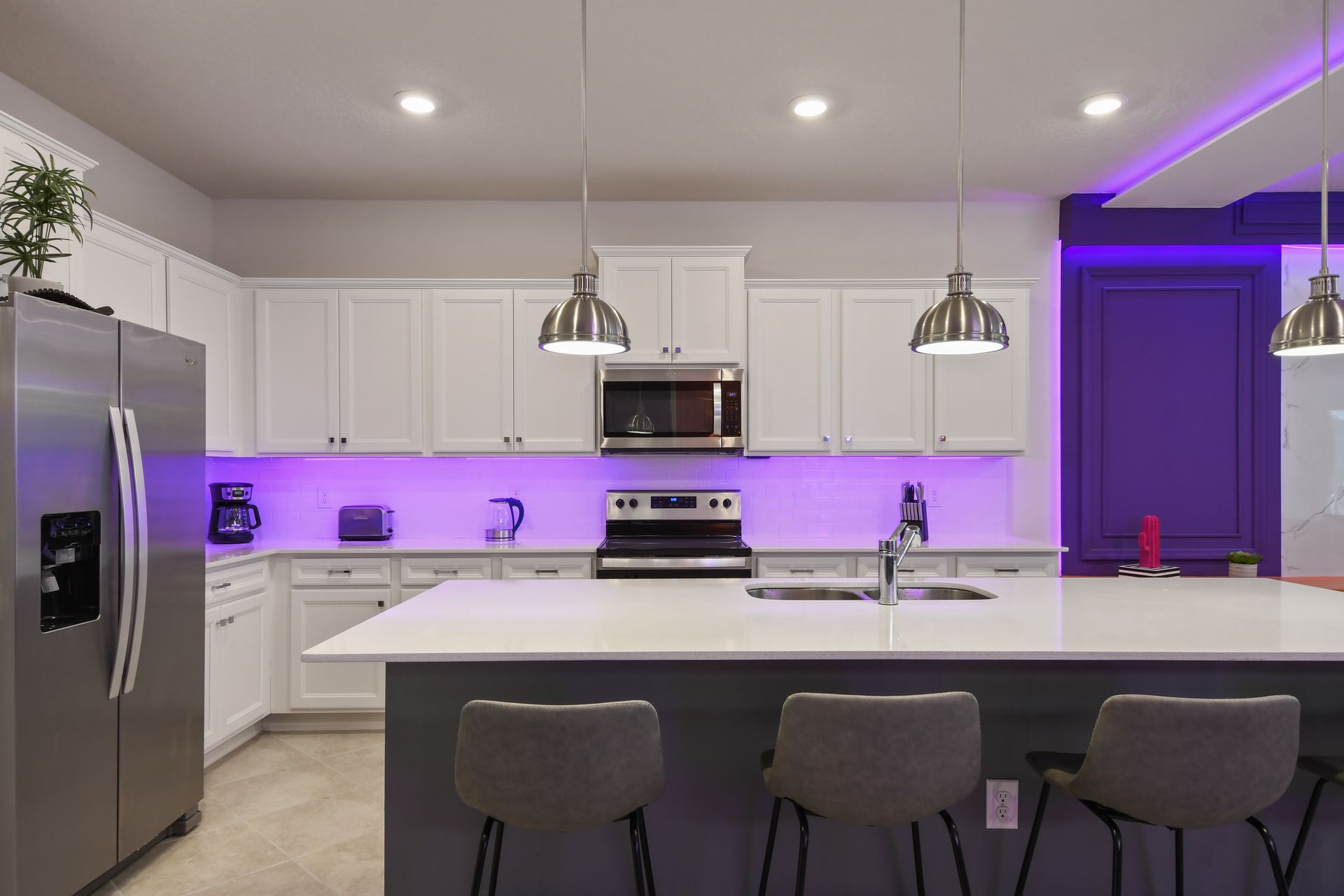 Contemporary kitchen with island seating, stainless steel appliances, and purple LED lighting.