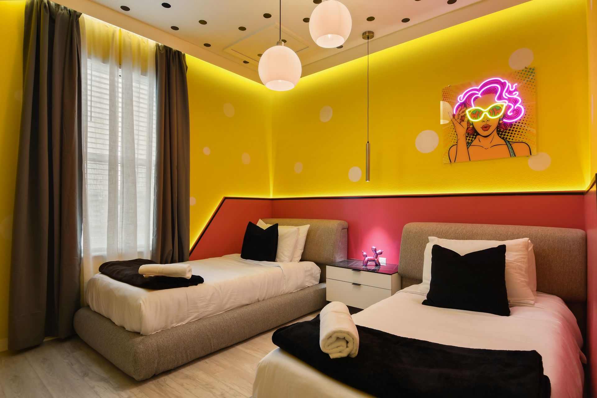 Vibrant bedroom with twin beds, pop art decor, and playful neon lighting.