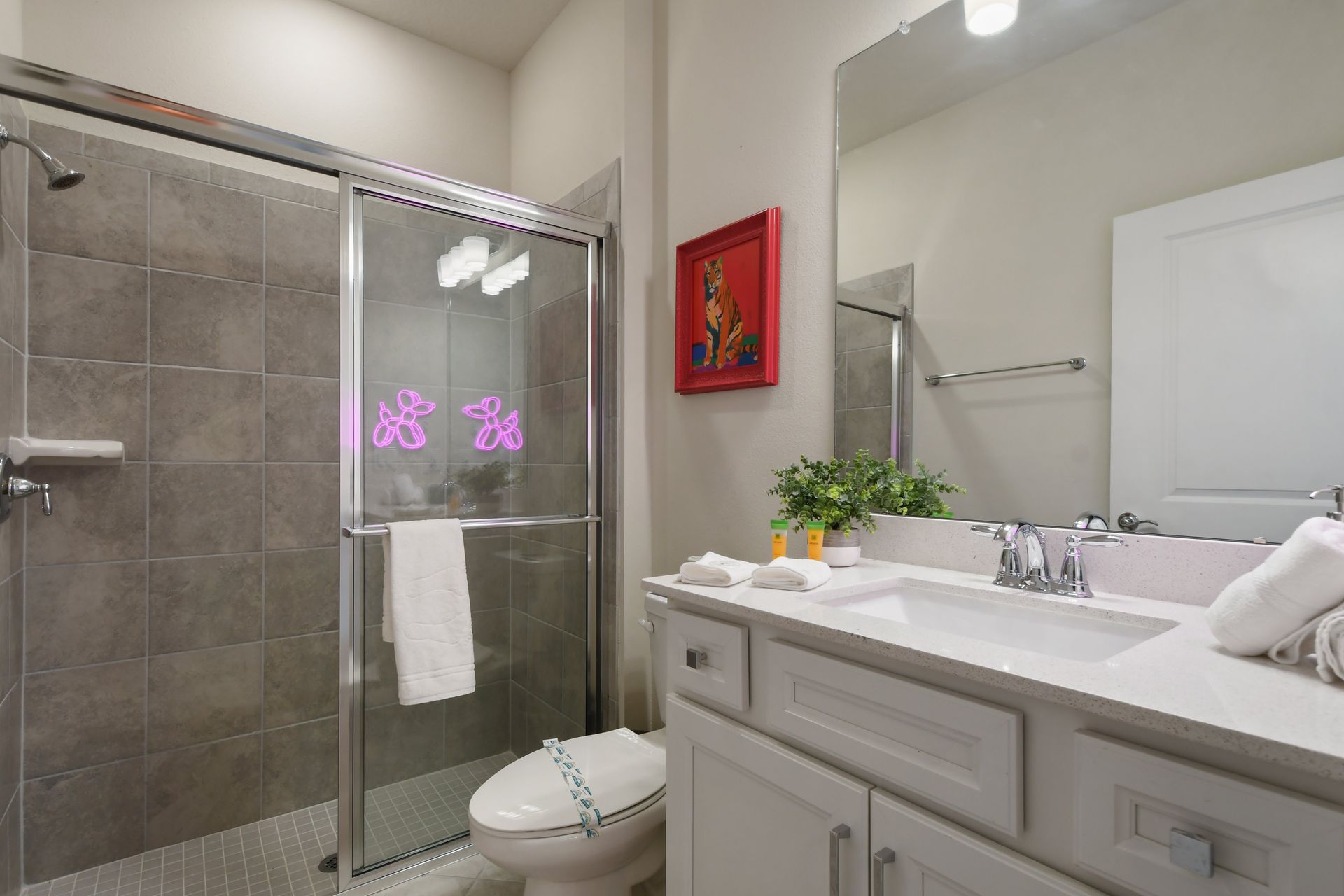Chic bathroom with a modern shower, vibrant art, and playful neon decor.
