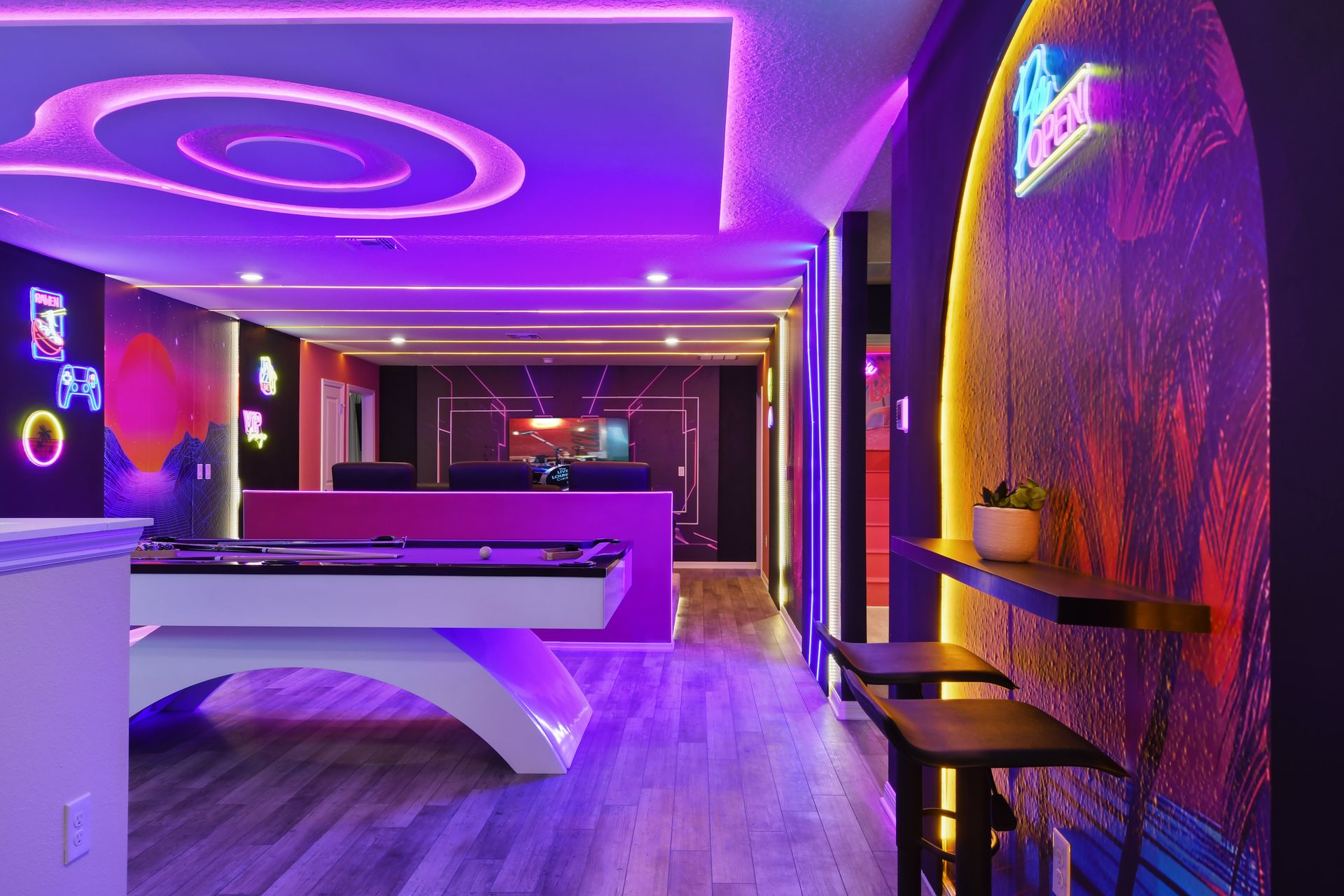 Neon-soaked game room with pool table, bar seating, and vibrant decor.