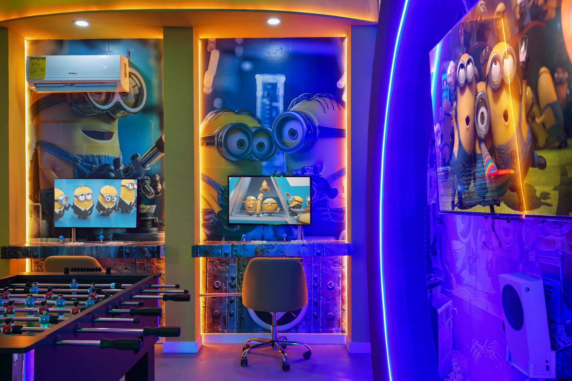 Minion-themed gaming room with neon lighting, foosball, and multiple screens.