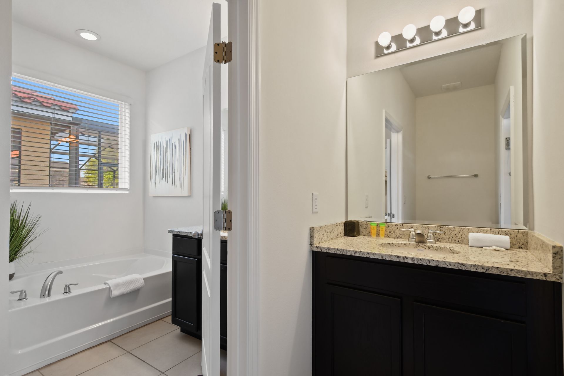 Spacious ensuite bathroom with granite vanity, large mirror, and soaking tub.