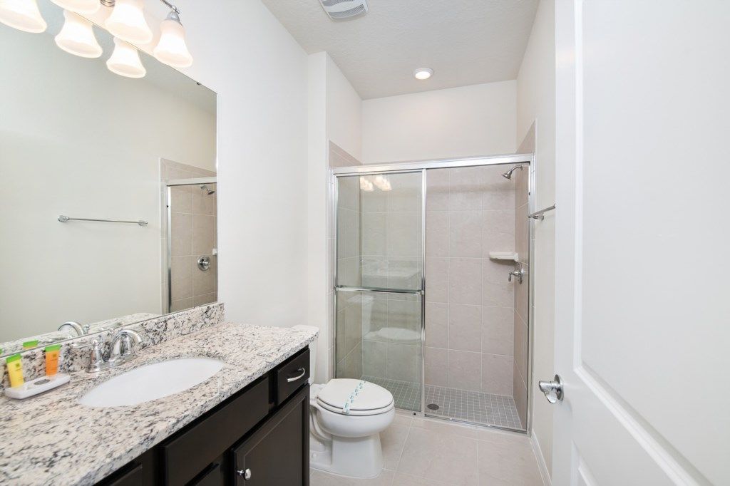 Modern bathroom with granite vanity, glass walk-in shower, and bright lighting.