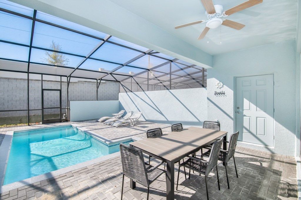 Private screened-in pool with lounge chairs, dining area, and ceiling fan comfort.