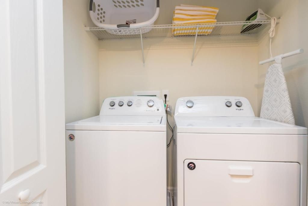 In-home laundry with washer, dryer, ironing board, and shelf storage.