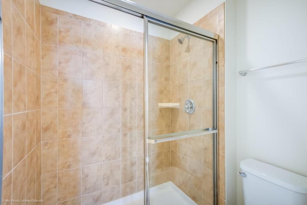 Spacious tiled walk-in shower with glass doors and built-in corner shelf.