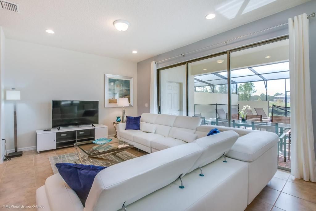Bright open living room with sleek sectional, large TV, and poolside views.
