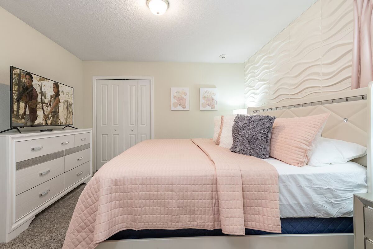 Chic pastel bedroom with textured walls, soft bedding, and a large smart TV.