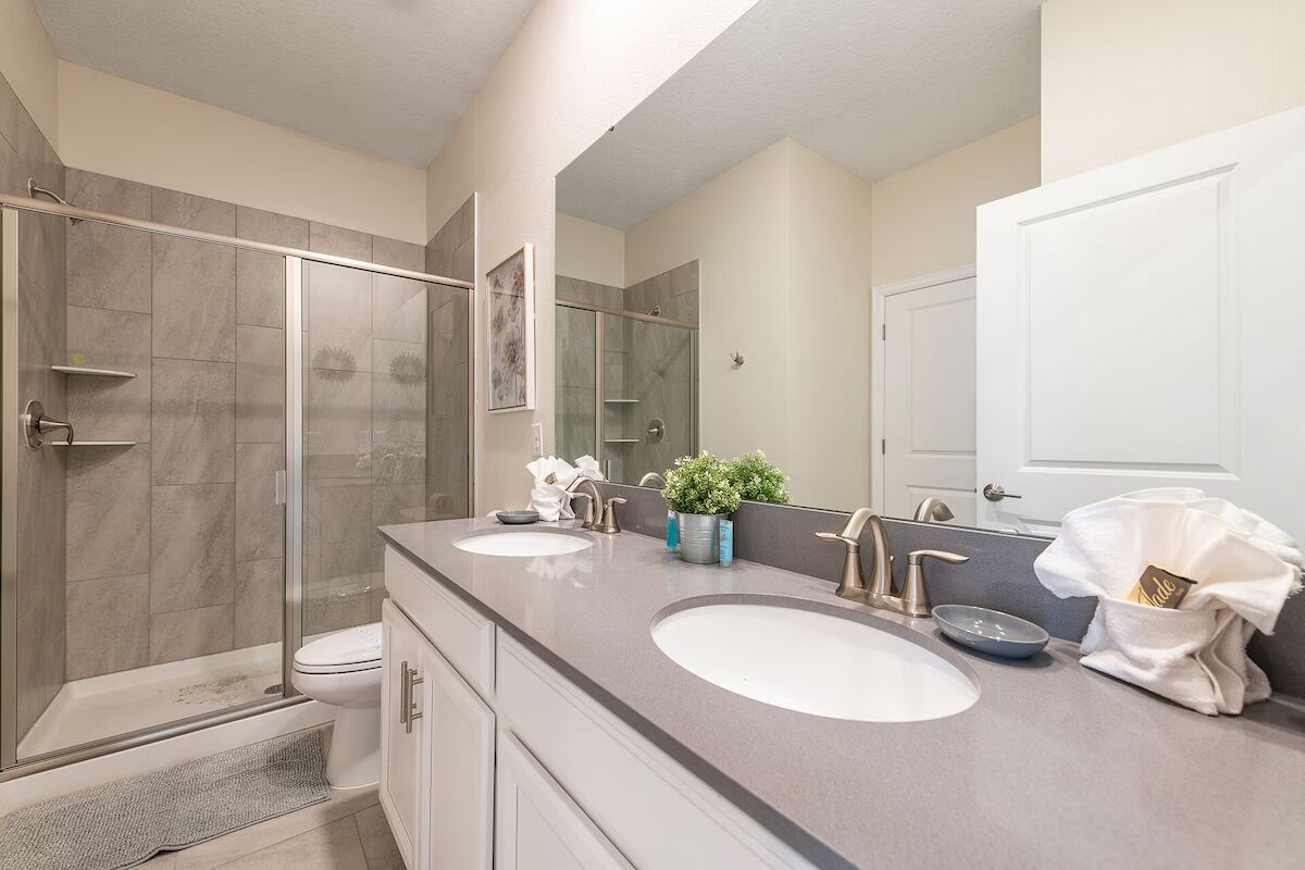 Contemporary bathroom with dual sinks, large mirror, and sleek glass walk-in shower.